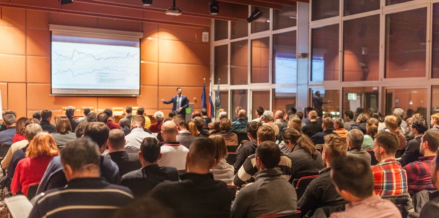 A speaker addressing a large audience in a conference hall.